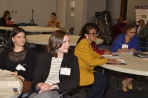 Attendees engaged in a meeting, focusing on discussions and note-taking at round tables.