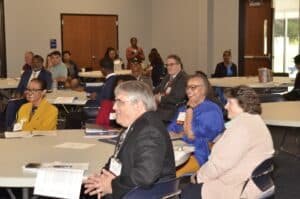 Participants engaged in a meeting, smiling and interacting at tables with documents in a conference room setting.