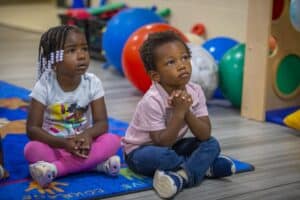 Children sitting on a colorful rug in a playroom with large exercise balls in the background.