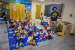 Young children attending a classroom activity with teacher and educational toys.