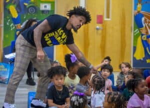 Teacher engaging children in classroom activity with colorful mural background.