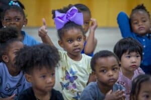 Children engaged in an activity, with one girl in a yellow shirt and purple bow giving a thumbs up.