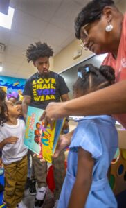 A group of children engage with an adult reading a colorful book about self-identity and representation.