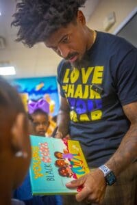 An author signs a children's book titled "Young Black Girl" while attentively interacting with young readers.