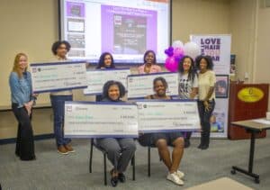 Eight participants hold large scholarship checks at an event promoting hair care and wellness.