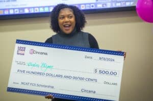 A joyful young woman holds a big check for $500, celebrating her NCAT FCS Scholarship award.
