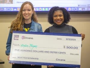 Two women proudly hold a large scholarship check for $500, celebrating an achievement.
