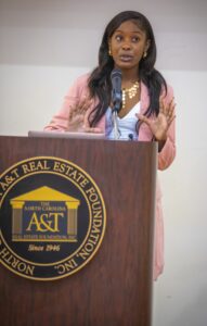 A woman in a pink blazer speaks at a podium with the North Carolina A&T Real Estate Foundation logo.