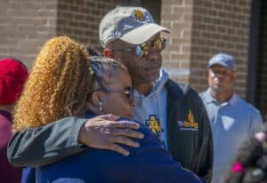 Empathetic hug between two individuals at a community event outdoors.