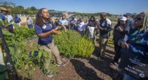 A woman giving a gardening demonstration to a group of people outdoors.