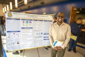 Young man presenting research poster at academic conference in a modern venue.