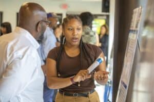 A woman explaining information on a digital display to a man at a conference or event.