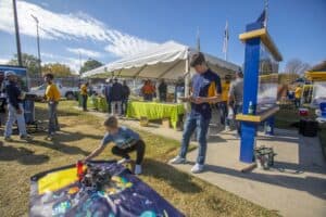 Children exploring robotics at outdoor tech event with tents and informational displays.