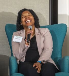 Enthusiastic woman speaking at a conference, smiling and holding a microphone.