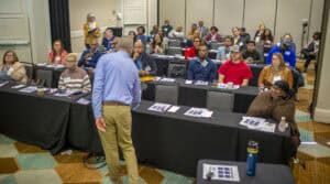 A seminar or conference with diverse attendees listening to a speaker at the front.