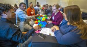 Attendees at the 2024 Grassroots Leadership Conference participate in a hands-on activity with colorful Lego blocks during a workshop session. Seated at a table, they engage in discussion and collaboration, surrounded by conference materials.