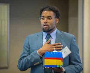 LEGO block presentation at a professional event with speaker Alex in a blue suit.