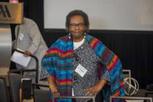 African American woman wearing a colorful shawl at a conference, smiling and posing for the camera.