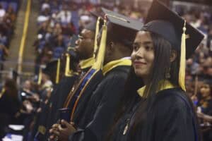 Graduate students in caps and gowns line up during commencement. Pictured in the foreground is Sukunya Poddar, a food and nutritional sciences major, smiling confidently while holding her diploma.