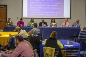 A panel of seven individuals, including Dr. Uzo as moderator, sits at a long table during a panel discussion on soil health. The panelists, dressed in formal attire, are engaged in discussion while attendees watch from round tables in the foreground.