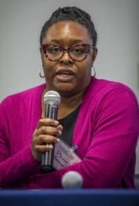 A woman identified as Porche Spence, wearing glasses and a magenta sweater, speaks into a microphone during a panel discussion at the World Soil Day Celebration.