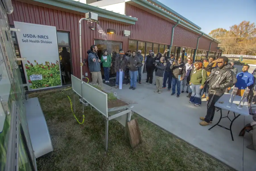 People gathered outside a building with a USDA-NRCS Soil Health Division sign, attending an outdoor.