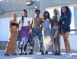Six individuals pose confidently in stylish outfits, showcasing diverse fashion against an urban backdrop.