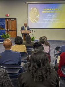 A speaker addresses an audience during the dedication of the Arthur P. Bell Conference Room at a university.