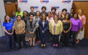 A diverse group of 20 people stand and smile for a group photo in front of an NC Cooperative Extension banner in an indoor setting.