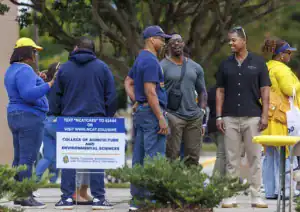 A group of people is gathered outdoors, chatting and smiling. A sign for the College of Agriculture and Environmental Sciences is visible nearby, indicating a university event.