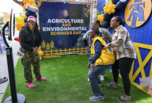 Four people smiling and posing playfully in front of a backdrop that promotes Agriculture and Environmental Sciences Day, surrounded by balloons.