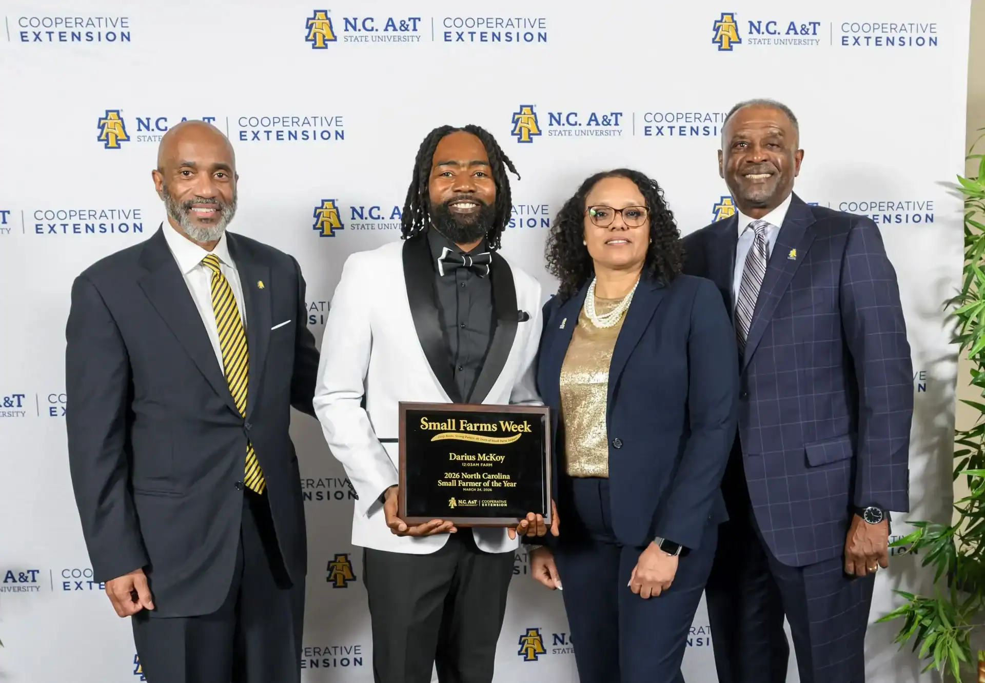 A group of four people pose for a photo, celebrating Darius McKoy, who holds a plaque recognizing him as the 2026 North Carolina Small Farmer of the Year during Small Farms Week.