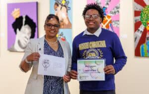 Celebrating achievement at CAES News art event with student holding first place certificate.