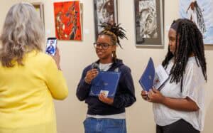 A woman taking a photo of two young women at an art gallery.