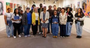 A diverse group of people at an art gallery, holding notebooks and smiling for the photo.