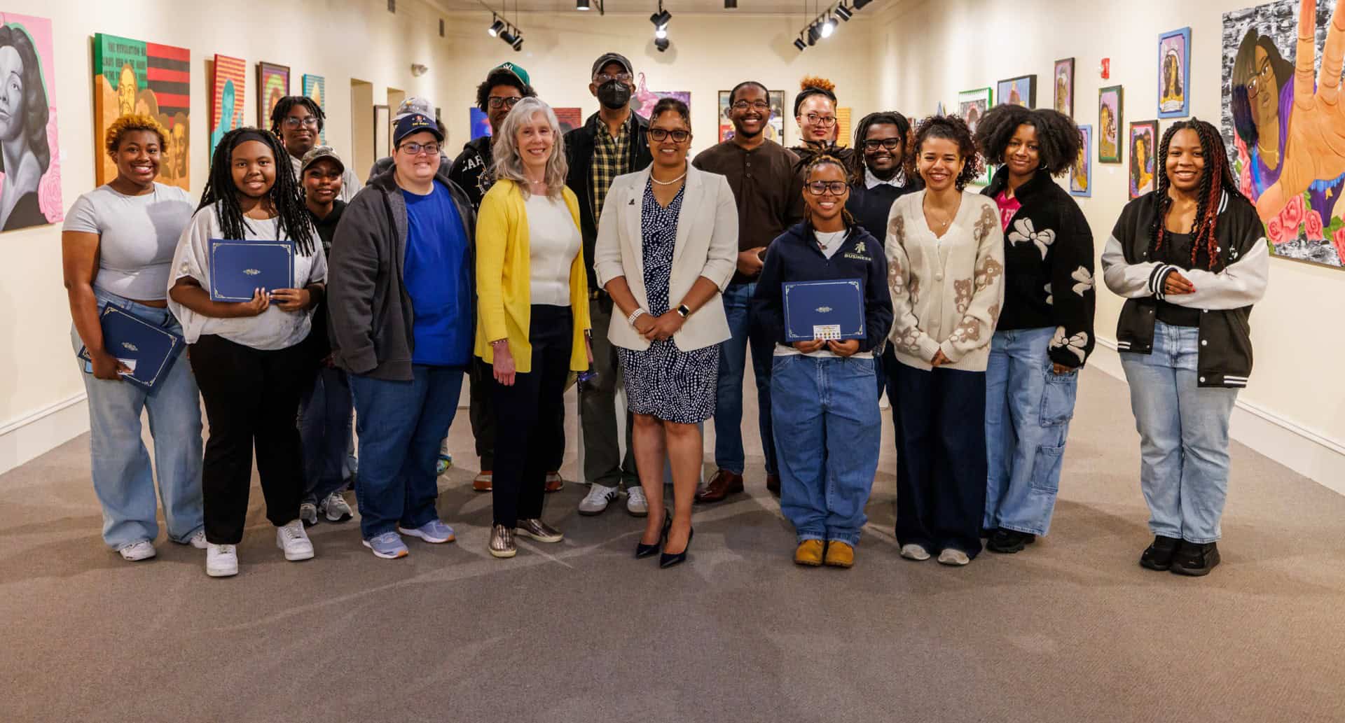 A diverse group of people at an art gallery, holding notebooks and smiling for the photo.
