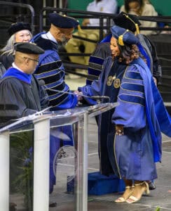 Graduation ceremony with graduates in academic regalia receiving diplomas at a university event.