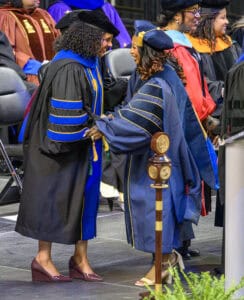 Graduates shaking hands during a university commencement ceremony in academic regalia.