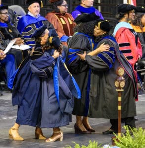 Graduates in academic regalia embracing during graduation ceremony at CAES News event.