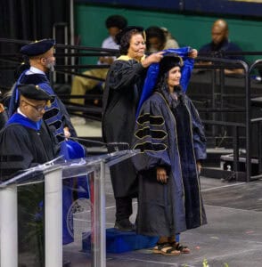 Graduation ceremony with students in academic regalia on stage at university event.