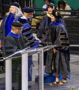 Graduation ceremony with students in academic regalia receiving diplomas on stage at university.