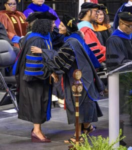 Graduates in academic regalia exchanging congratulations at graduation ceremony.