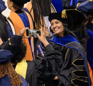 Graduation ceremony with smiling graduate taking photo in cap and gown at commencement event.