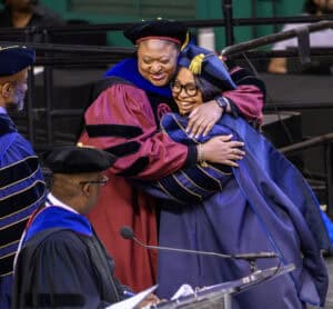 Celebrating graduation with joyful hugs at a university ceremony.