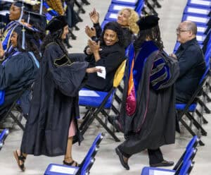 Graduates celebrating at a university graduation ceremony with faculty members and friends.