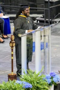 Graduation speaker at commencement ceremony delivering speech in cap and gown.