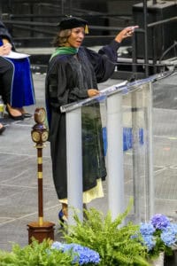 Graduation speaker delivering speech at university commencement ceremony with academic regalia.
