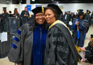 Graduates celebrating at a graduation ceremony, wearing caps and gowns, smiling and embracing each o.