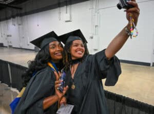 Graduates taking a selfie at graduation ceremony in caps and gowns.