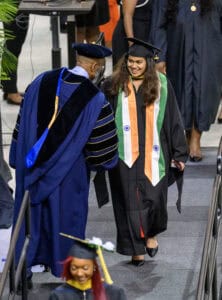 Graduation ceremony with smiling female graduate receiving diploma from faculty member.